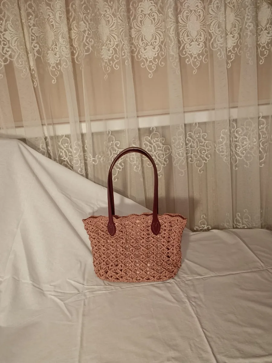 Pink raffia bag on a bed sheet in front of a curtain